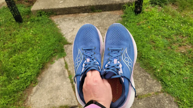 A person holds up a pair of Saucony Guide 19 shoes.