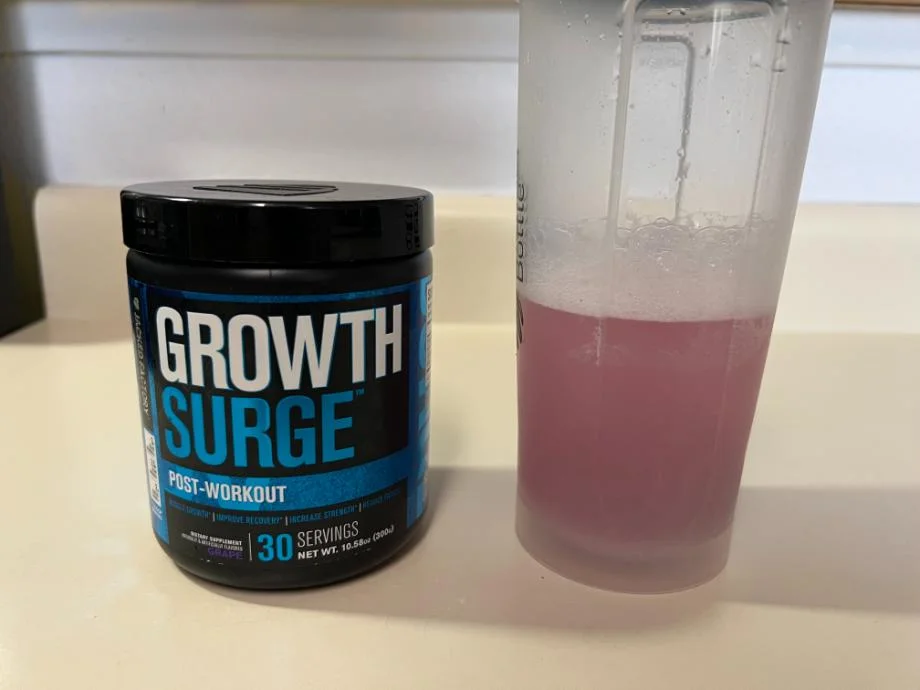 A freshly mixed shaker cup of Jacked Factory Growth Surge rests next to the container.