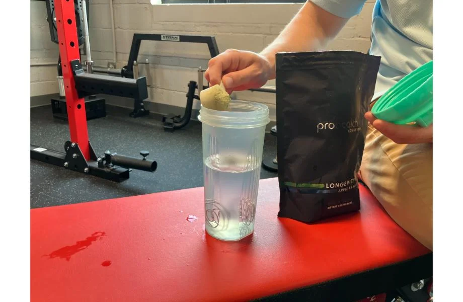 man_scooping_pro_health_longevity_greens_into_shaker_cup