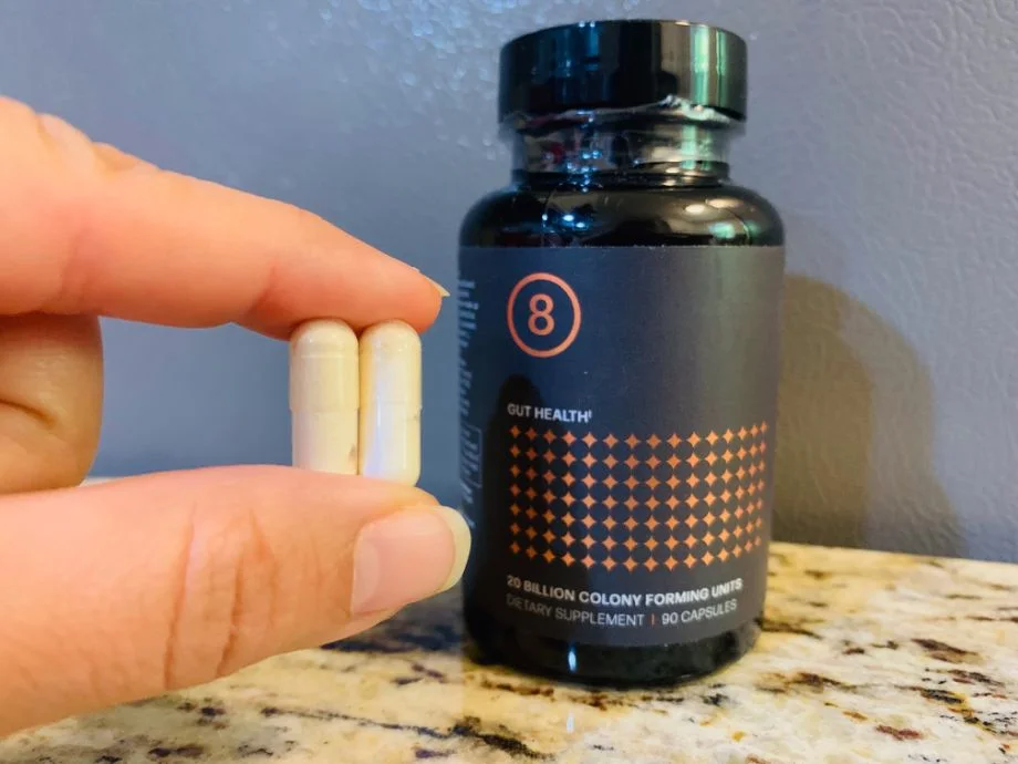 Person holding a serving of two capsules next to a container of Biotics 8