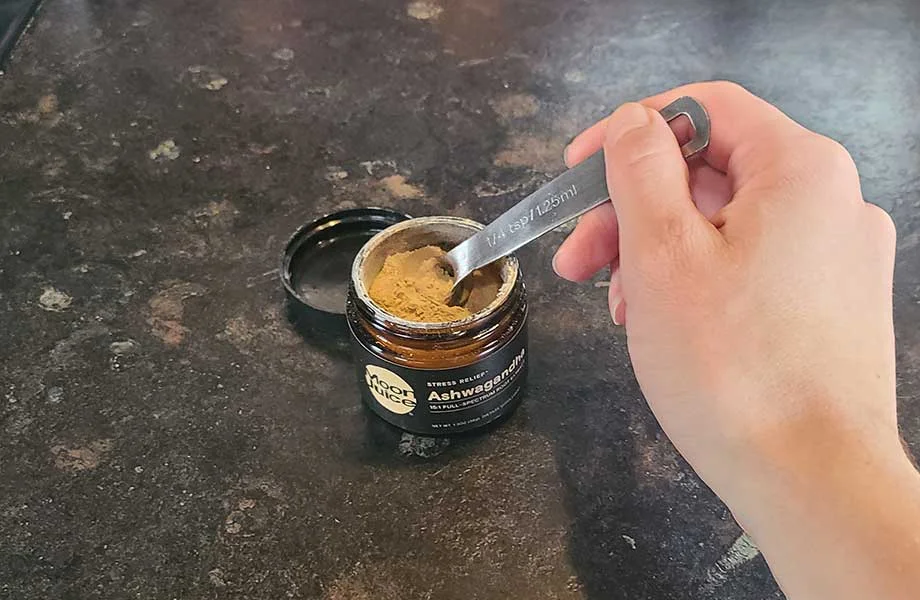 A person scoops a bit of Moon Juice Ashwagandha Powder out of its container