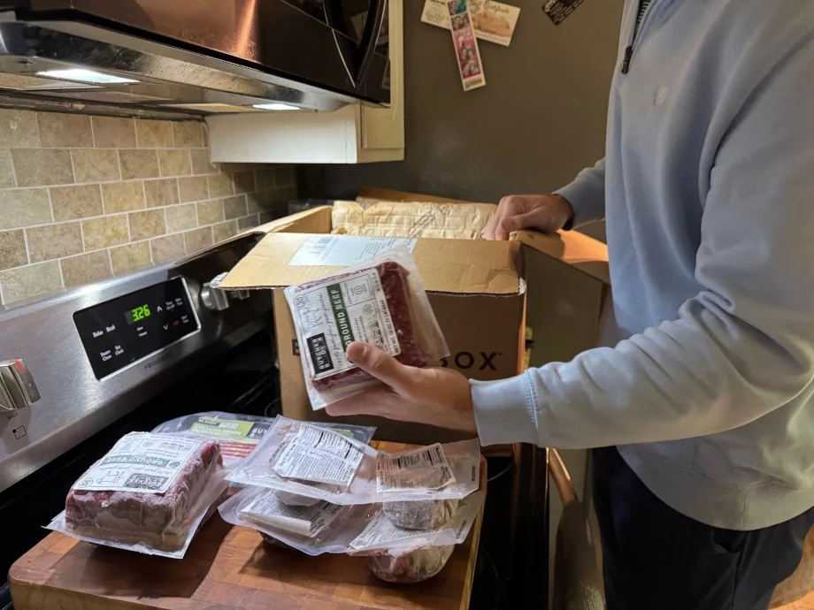 A person takes items from a ButcherBox package and sets them on a cutting board.