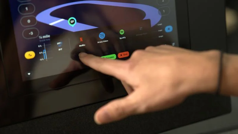 A hand reaches out to select a streaming service on the NordicTrack Commercial 1250 treadmill display.