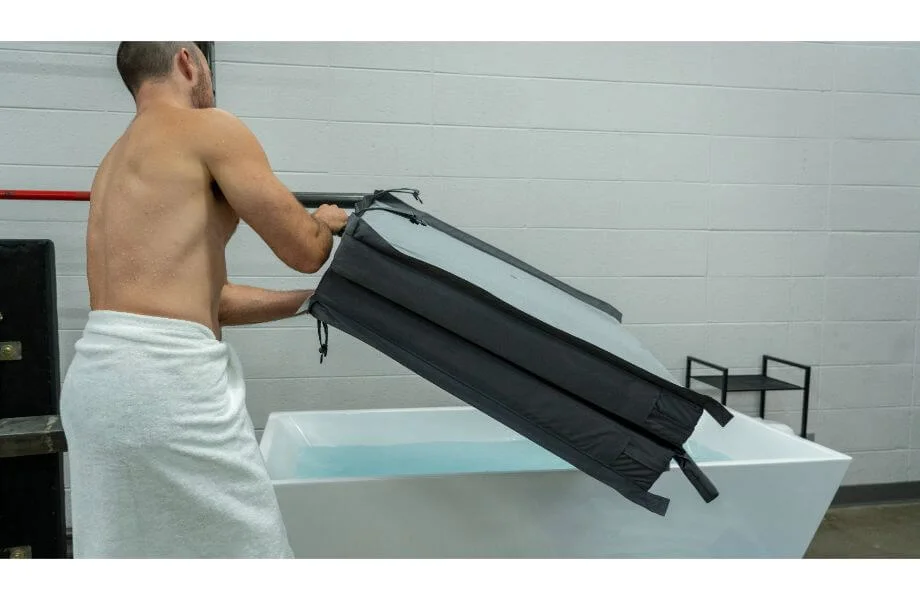 Man with a white towel around his waist putting the cover on a cold plunge tub