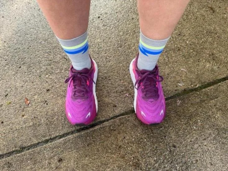 A person wearing purple running shoes paired with the Feetures Elite Light Cushion Mini Crew Socks in grey with neon yellow and blue bands