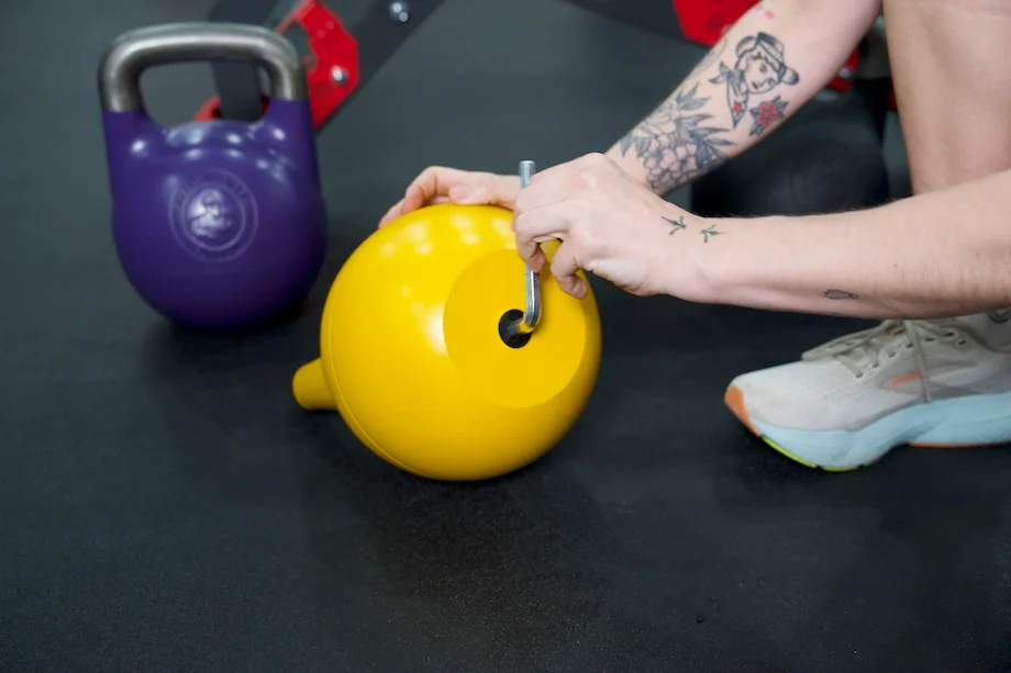 A woman adjusts the Bells of Steel Adjustable Kettlebell using an allen wrench
