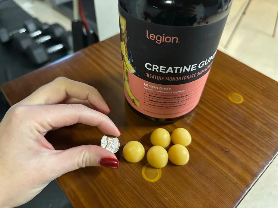 A woman holding a nickel next to five Legion Creatine Gummies to show the size comparison.