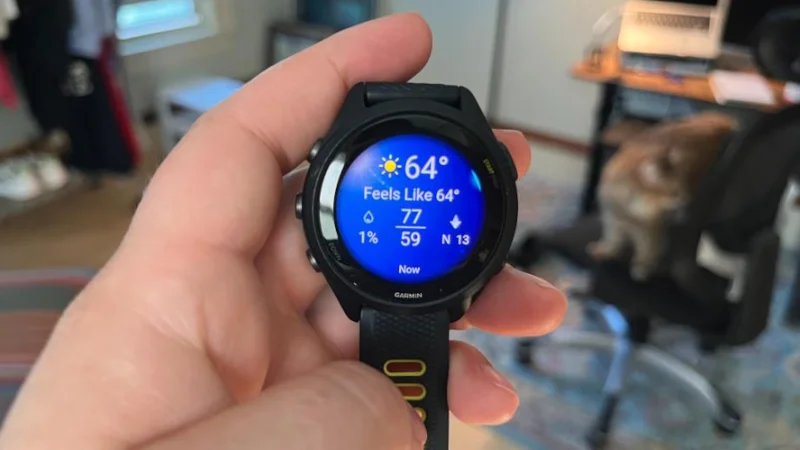A woman holds up a Garmin Forerunner 265 to display the watch face.