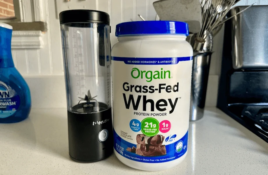 A container of Orgain Grass-Fed Whey Protein next to a portable blender