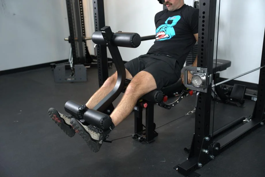 Man performing leg extensions using the GLEG Weight Bench on the Body-Solid Functional Trainer Rack