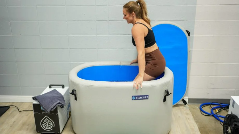 A woman wearing workout clothes getting into an Inergize ice bath tub