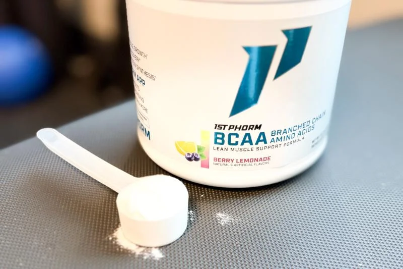 A scoop of 1st Phorm BCAAs next to its container