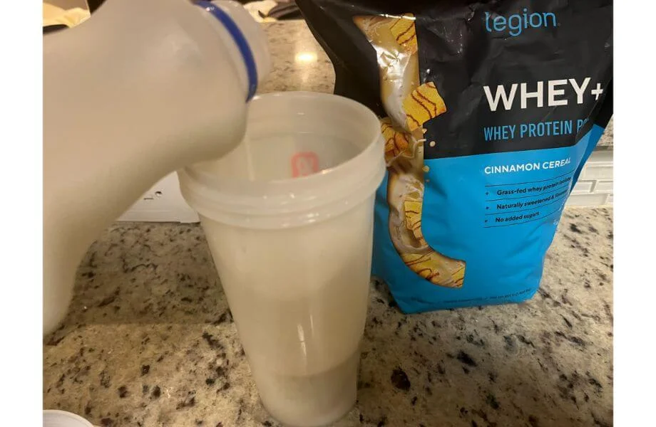 Person pouring milk into a shaker cup with Legion Whey+