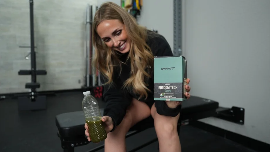 Woman holding a box of Onnit Shroom Tech Greens and a bottle with the mixed drink