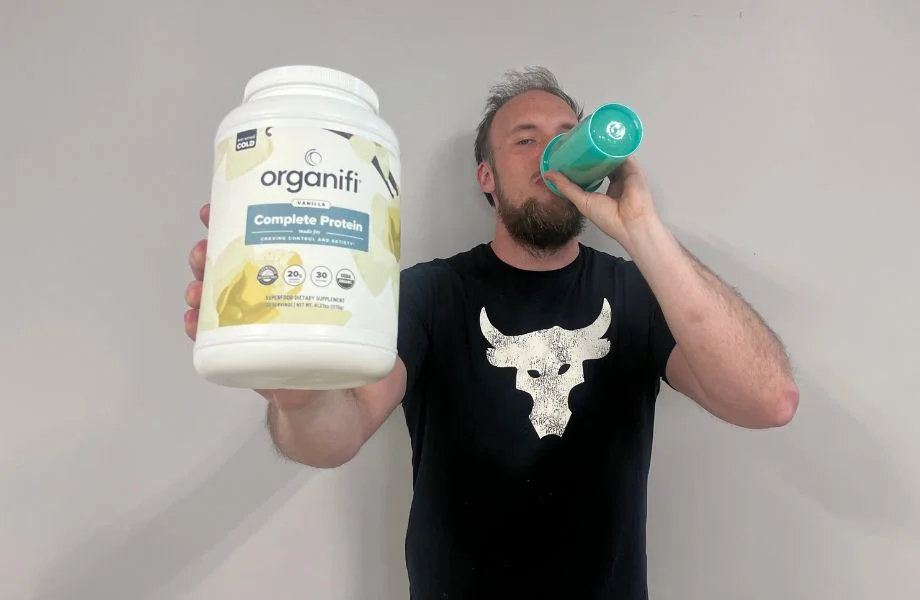 Man drinking Organifi Complete Protein and holding the container