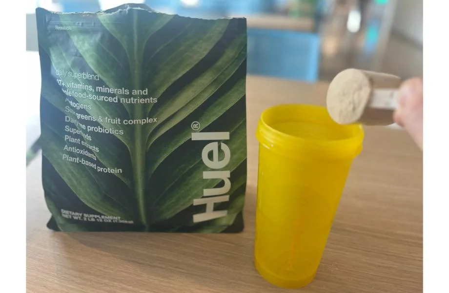 Huel daily superblend being scooped into a yellow shaker cup