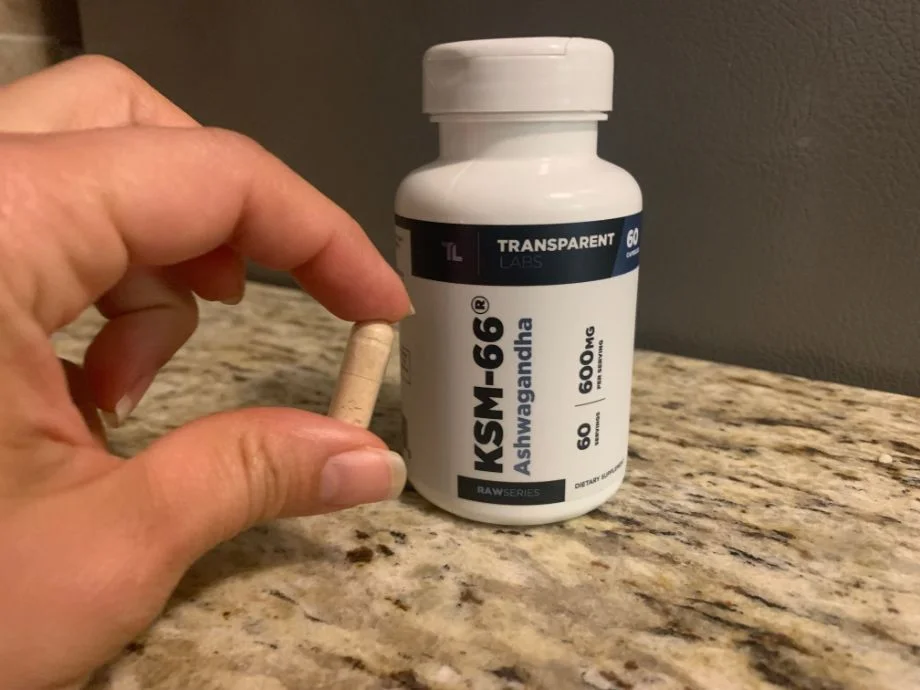 A person holding a single pill in front of a bottle of Transparent Labs Ashwagandha