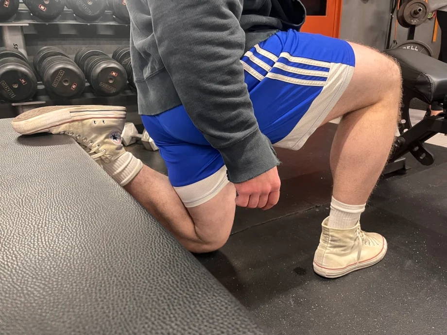 A man squats with a weight bench wearing Converse Chuck Taylor shoes.&nbsp;