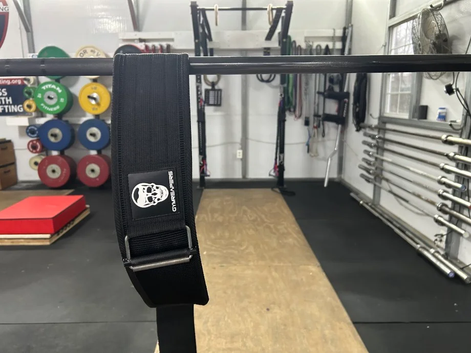 A Gymreapers Quick-Lock Belt is shown hanging from a bar in a gym.