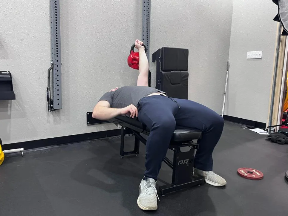 A man using a PRx Profile Folding Bench to perform single-arm kettlebell presses