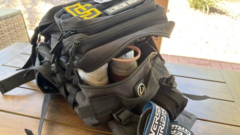 Gym bag essentials are spilling out of a gym back on a wooden patio table.