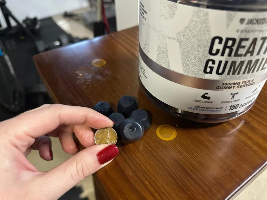 Our tester holds a penny up next to a Jacked Factory Creatine Gummy for size comparison.