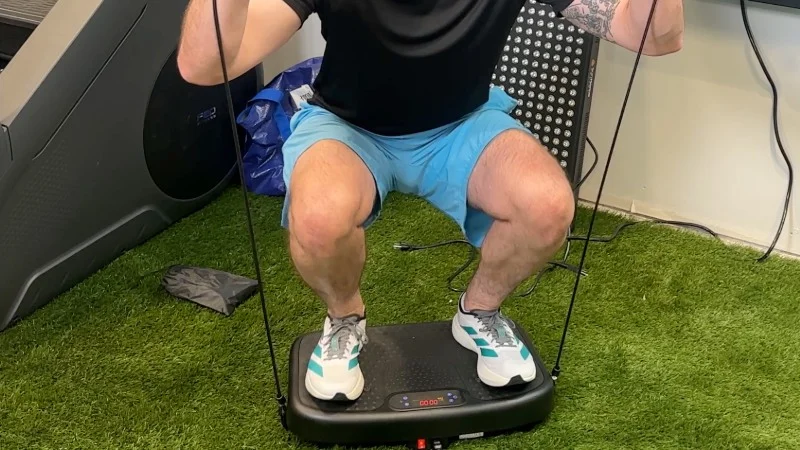 A person squatting with resistance bands on the SoftGym Vibration Plate