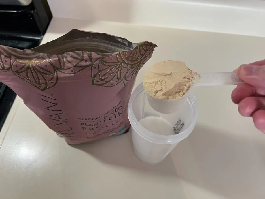 A scoop of Truvani Protein Powder about to be poured into a shaker cup