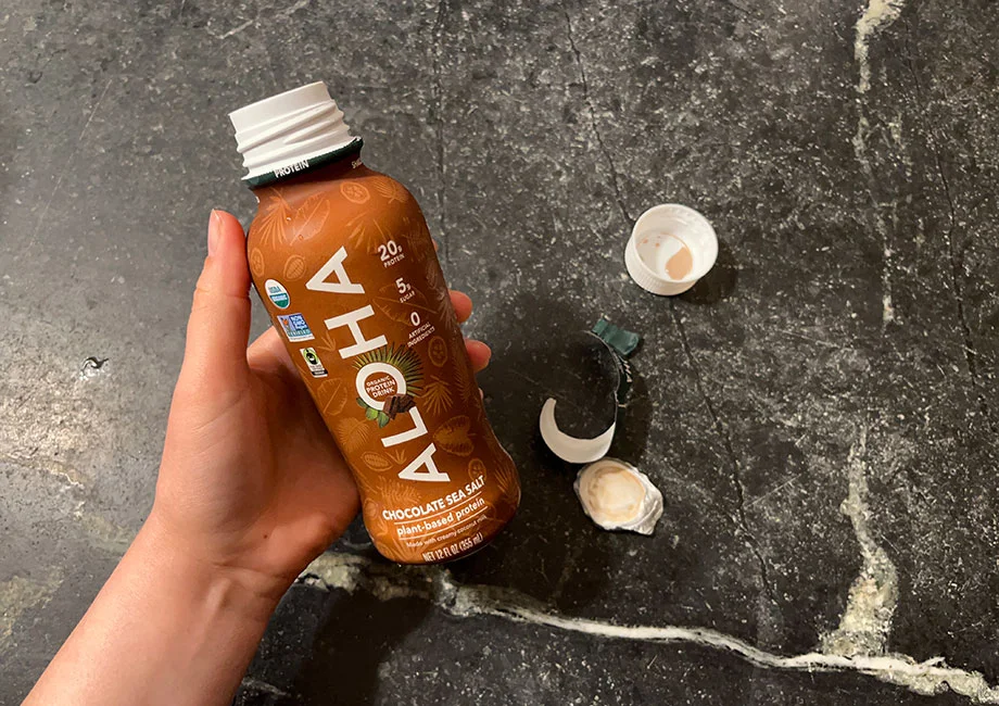 A close-up shot of an ALOHA chocolate sea salt protein shake bottle in a woman's hand.