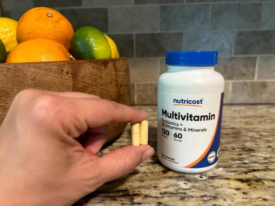 A hand holds up a few capsules of Nutricost Mulitvitamins next to the bottle.