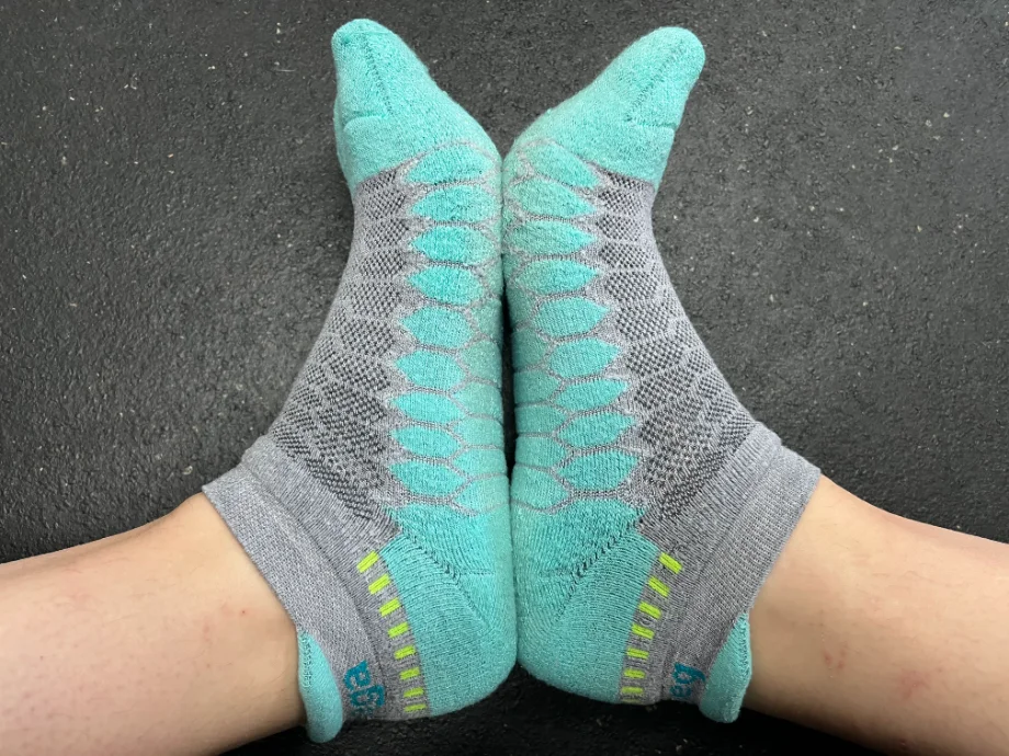 Close-up of a pair of feet in blue and grey  Balega Silver No-Show Compression-Fit Running Socks with green heel accents, emphasizing athletic design and fit.
