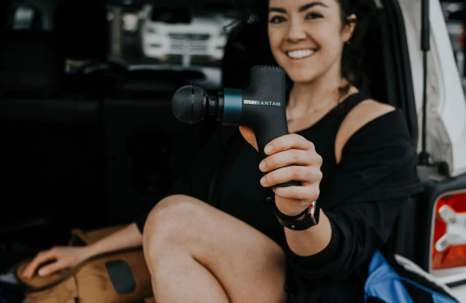 A smiling woman holds up an Ekrin Bantam mini massage gun