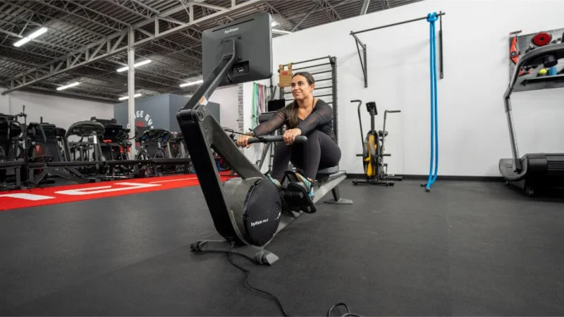 A woman in a gym setting using a Hydrow Wave rowing machine