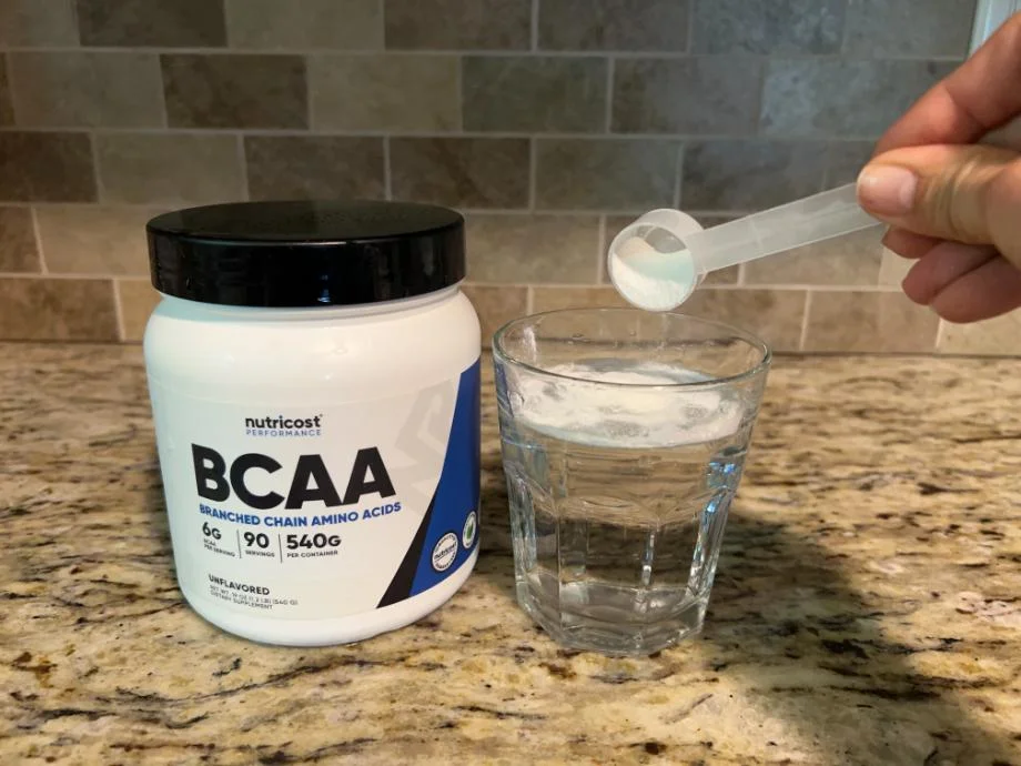 A person pours a scoop of Nutricost BCAAs into a glass of water.