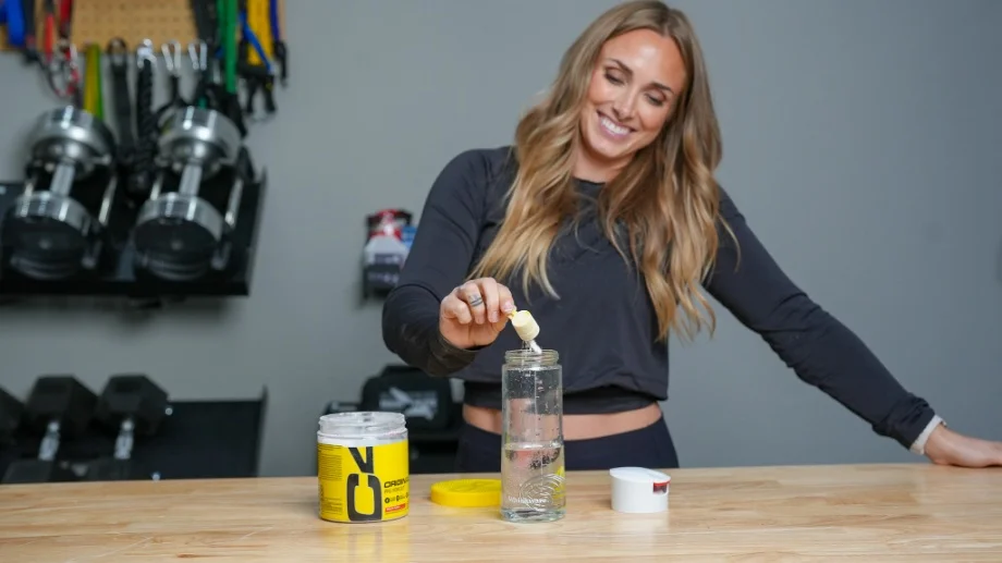 A woman pours a scoop of C4 pre-workout into a shaker bottle