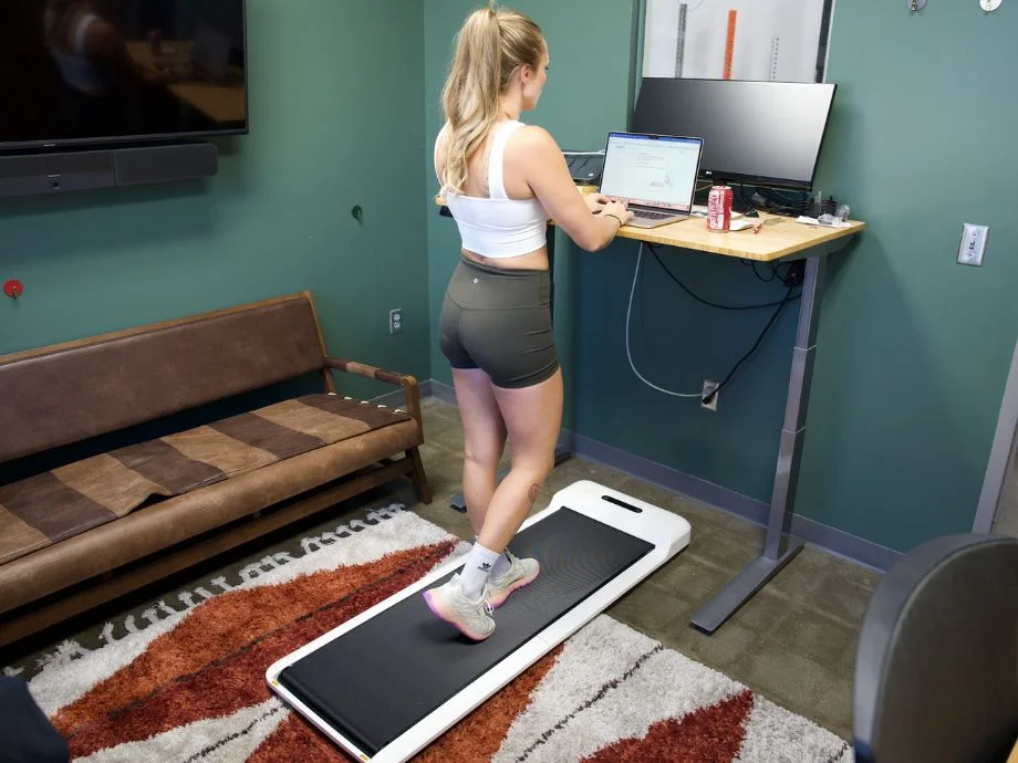 Blonde woman in workout clothes walking on a WalkingPad C2 while at a standing desk