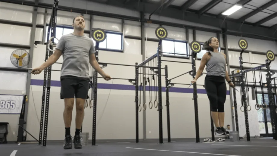 Action shot of a man and a woman jumping rope in a large gym.