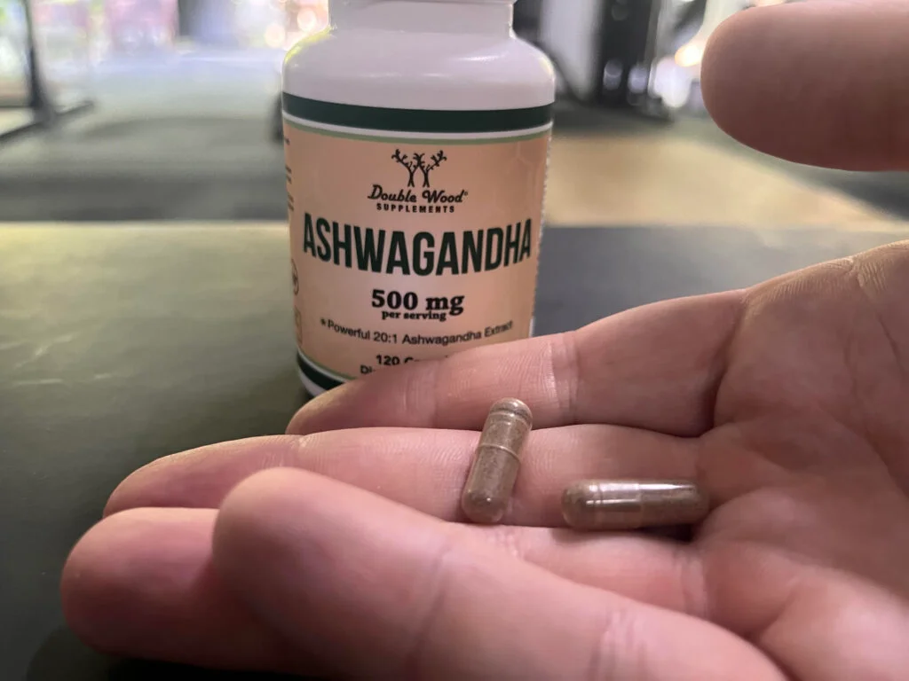 A hand holding a couple of Double Wood Ashwagandha pills in front of the container