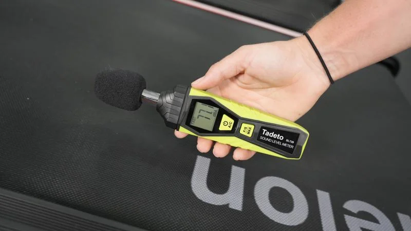 A person takes a decibal reading From the Echelon Stride 8s Treadmill.