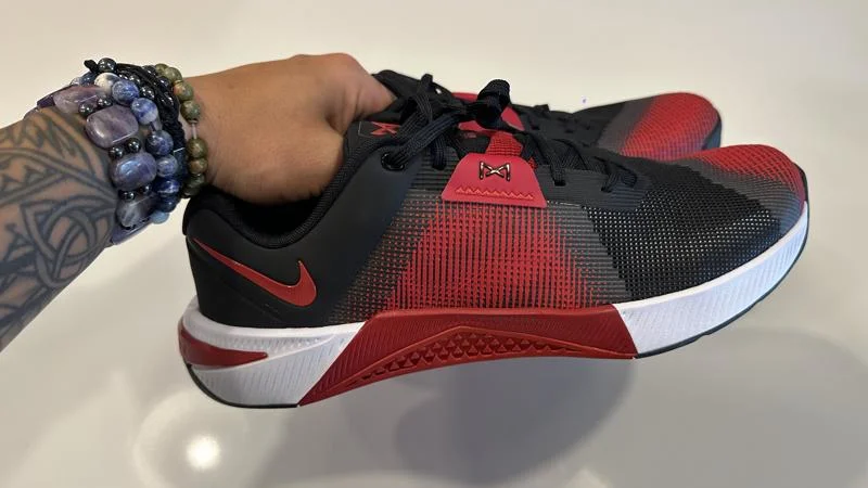 Holding up a pair of Nike Metcon 10 training shoes