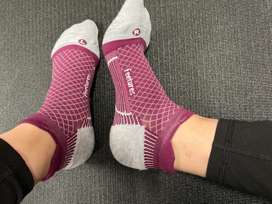 A close-up of feet wearing vibrant purple Feetures Plantar Fasciitis Relief Socks with grey toes, heels, and a dotted grid pattern, highlighting their design for enhanced comfort and support.
