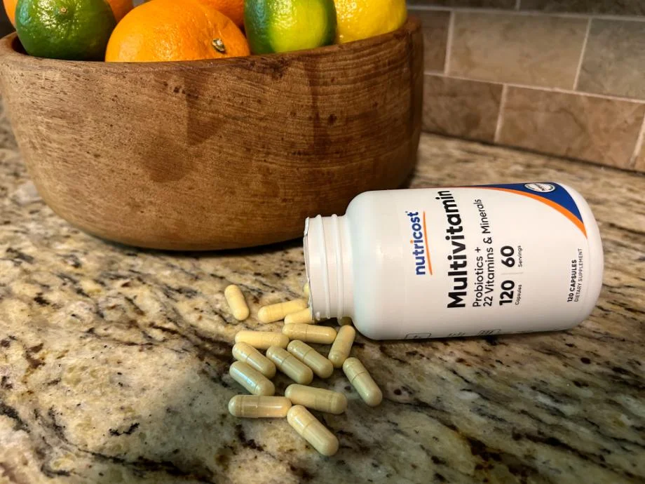 Close-up of open tipped-over bottle of Nutricost Multivitamins, with a handful of capsules filled with a yellowish powder spilling out.