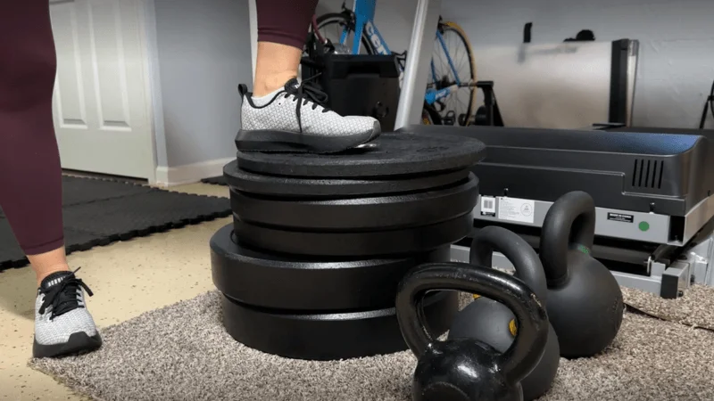 Our tester placing their foot on a stack of bumper plates in their home training center