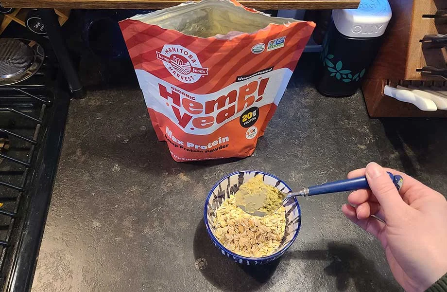 Dumping a scoop of Manitoba Harvest Hemp Yeah! protein powder into a bowl of oatmeal