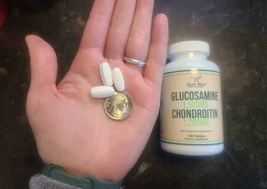 A person holds a few Double Wood Glucosamine Chondroitin Joint Supplement capsules with a quarter for size comparison.