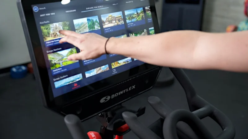 A person uses the touchscreen on a BowFlex Velocore bike.