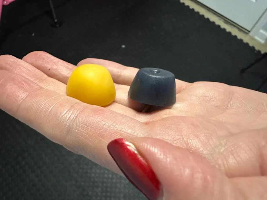 A hand holds a Legion Creatine Gummy next to a Jacked Factory Creatine Gummy, to compare the size of the two gummies