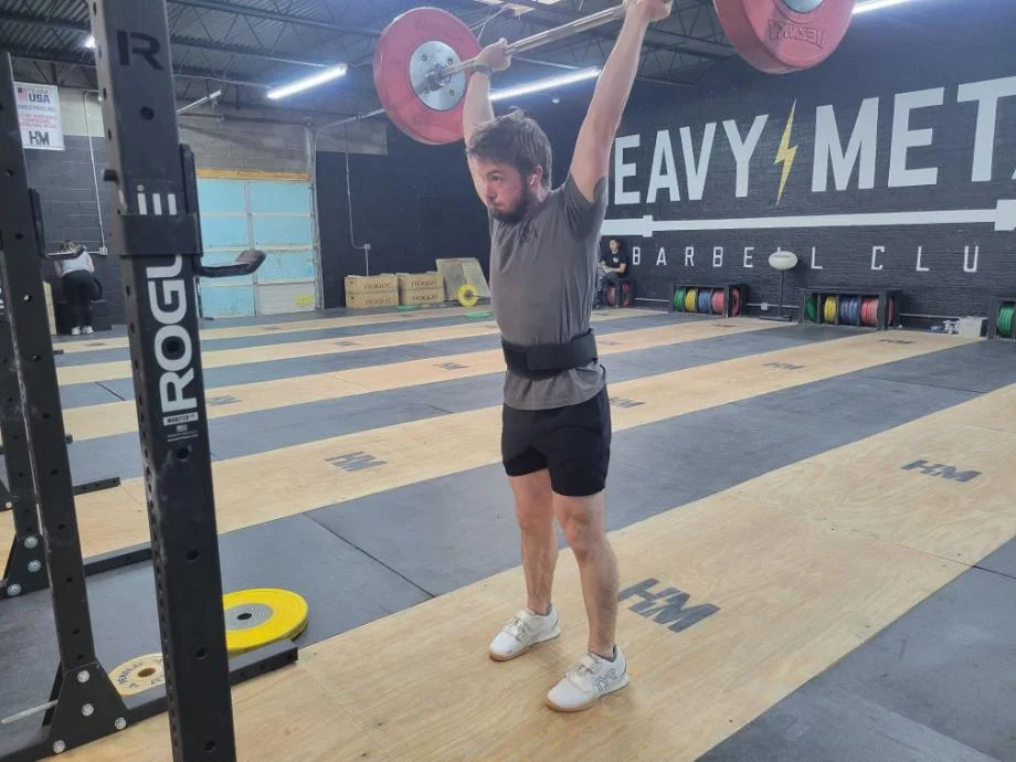 A man finishes a push press while using the Warm Body Cold Mind 4" Nylon Weightlifting Belt