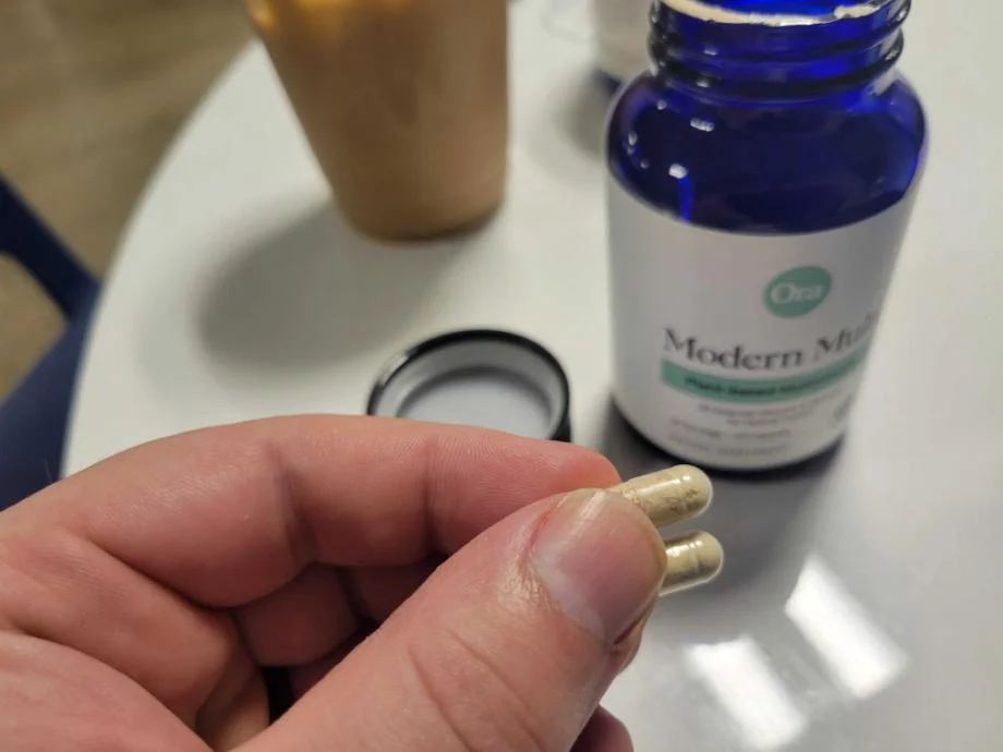 A person holding the two-capsule serving size of Ora Organic Modern Multi multivitamin