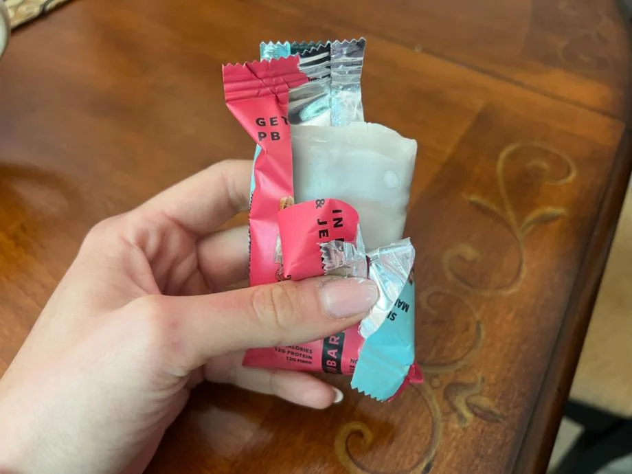 A hand holding an opened TRUBAR Protein Bar